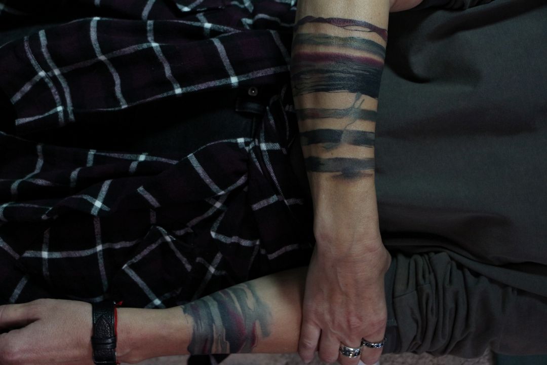 Abstract brushstroke tattoos on forearms with black and watercolor elements
